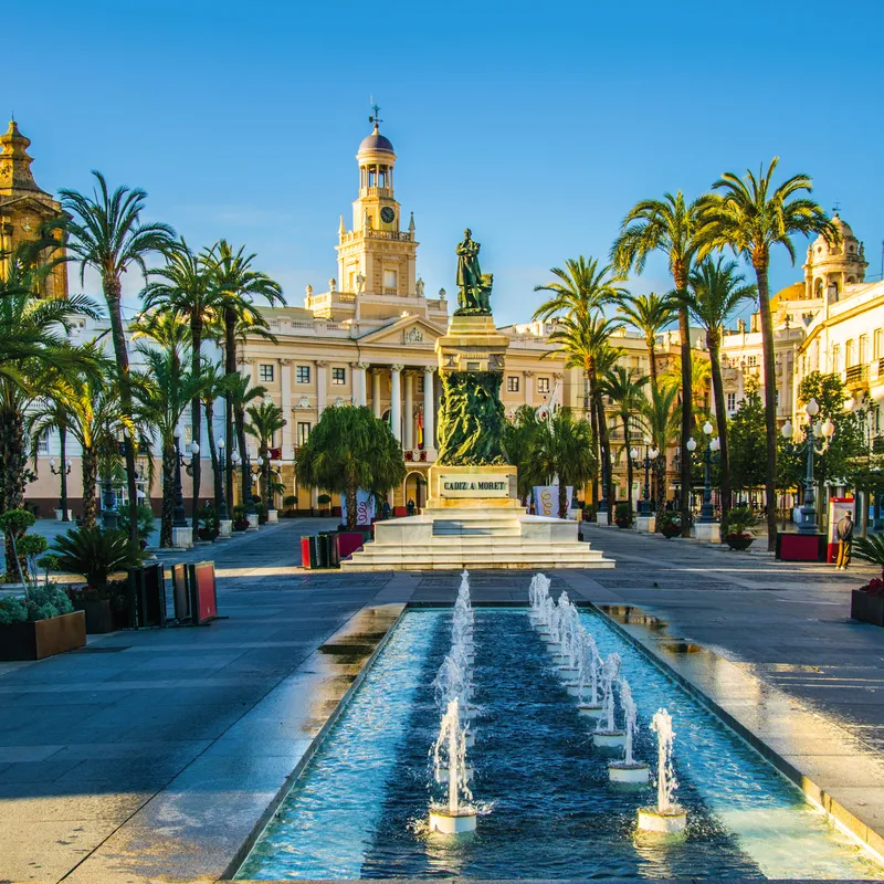 Stadtplatz von Cádiz mit Palmen und Springbrunnen bei sonnigem Wetter.
