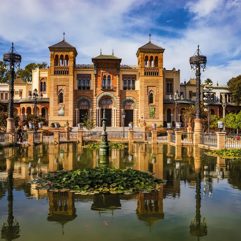 Historisches Gebäude mit reflektierendem Teich in Spanien, umgeben von Bäumen.