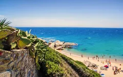 Strand mit Personen, blauem Meer und Kakteen an der Costa de la Luz, Spanien.