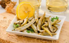 Frittierter Fisch mit Zitrone auf Teller, im Hintergrund zwei Gläser mit Getränken.