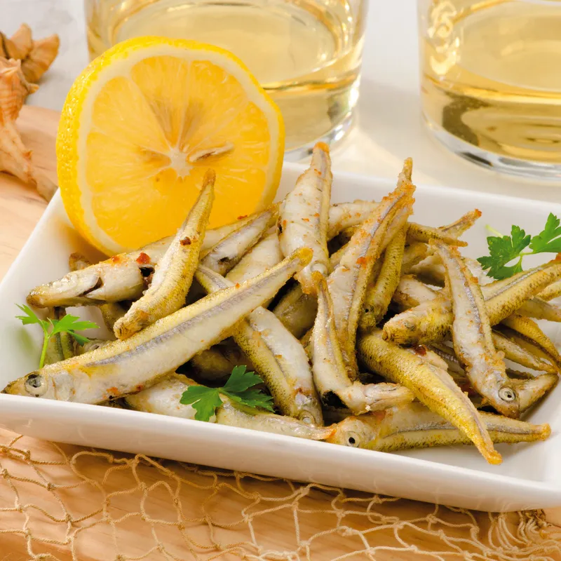 Frittierter Fisch mit Zitrone auf Teller, im Hintergrund zwei Gläser mit Getränken.