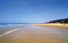 Weitläufiger Sandstrand unter klarem Himmel an der Costa de la Luz in Spanien.