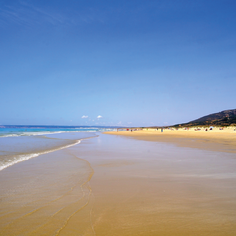 Weitläufiger Sandstrand unter klarem Himmel an der Costa de la Luz in Spanien.