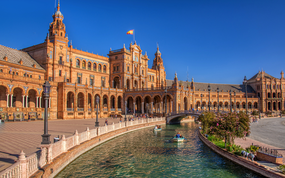 Plaza de España in Sevilla bei sonnigem Wetter mit Wasserkanal und Booten im Vordergrund.