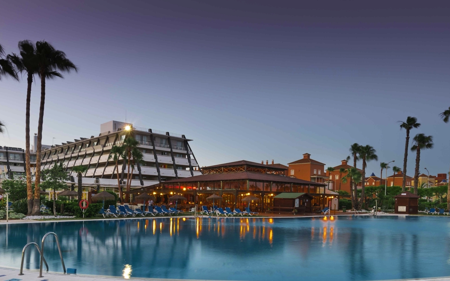 Hotelanlage mit großem Pool und Palmen bei Sonnenuntergang.