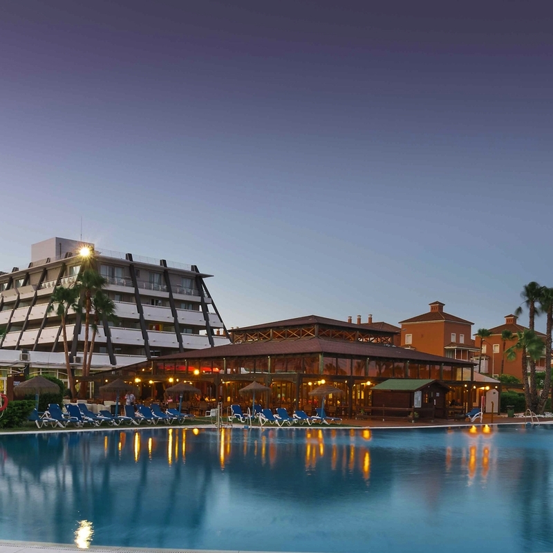 Hotelanlage mit großem Pool und Palmen bei Sonnenuntergang.