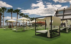 Grüne Terrasse mit Liegen und Sonnenschirmen vor einem modernen Hotelgebäude.