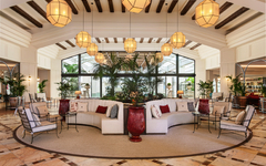 Hotel-Lobby mit weißen Sofas, Pflanzen und hängenden Lampen.