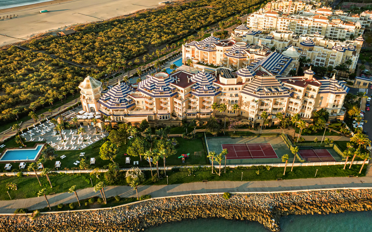Luftaufnahme eines Hotels mit Pool und Tennisplatz am Strand von Isla Canela, Spanien.