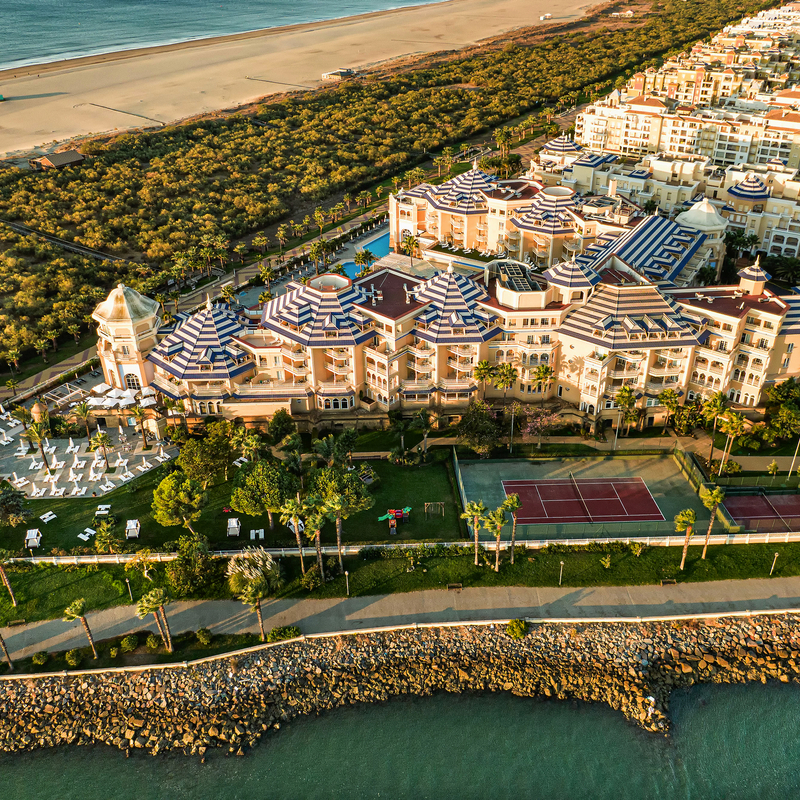 Luftaufnahme eines Hotels mit Pool und Tennisplatz am Strand von Isla Canela, Spanien.
