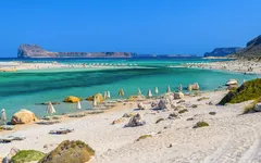Strand mit türkisfarbenem Meer und Sonnenschirmen an der Balos-Bucht auf Kreta.