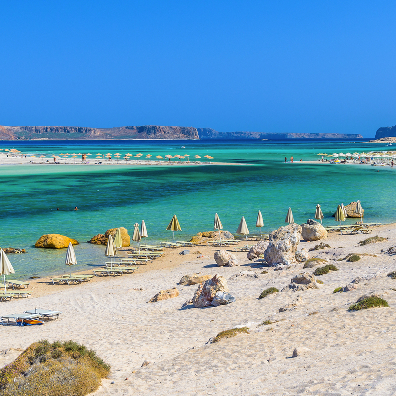 Strand mit türkisfarbenem Meer und Sonnenschirmen an der Balos-Bucht auf Kreta.