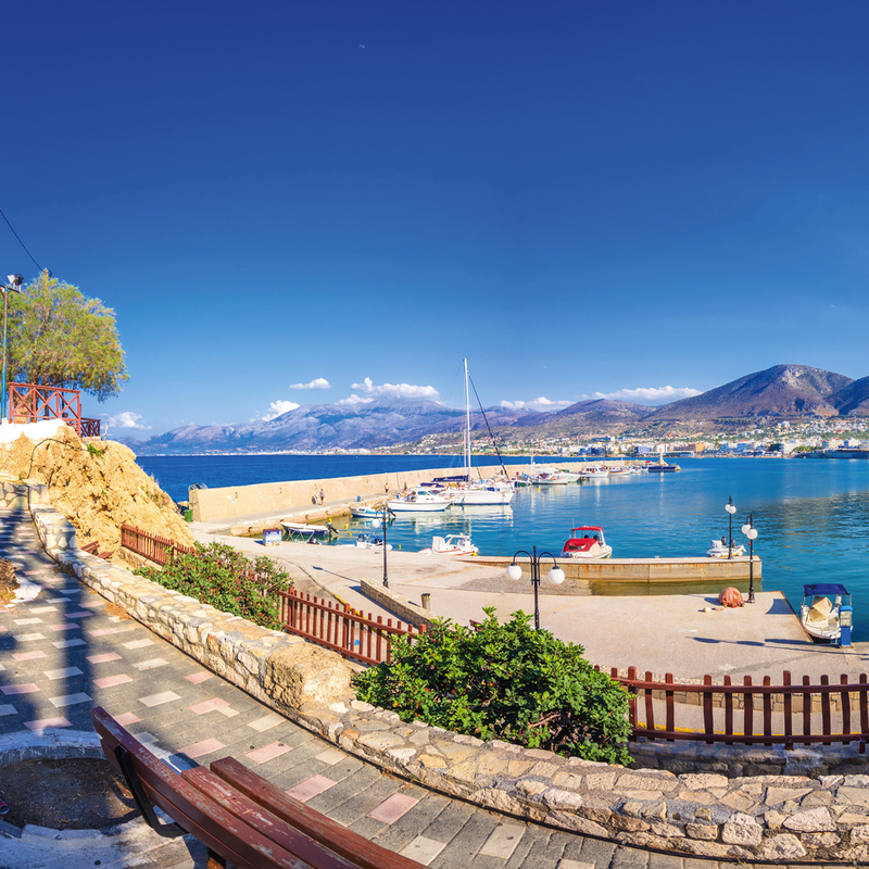 Hafen von Chersonissos auf Kreta mit Booten und hügeliger Landschaft im Hintergrund.