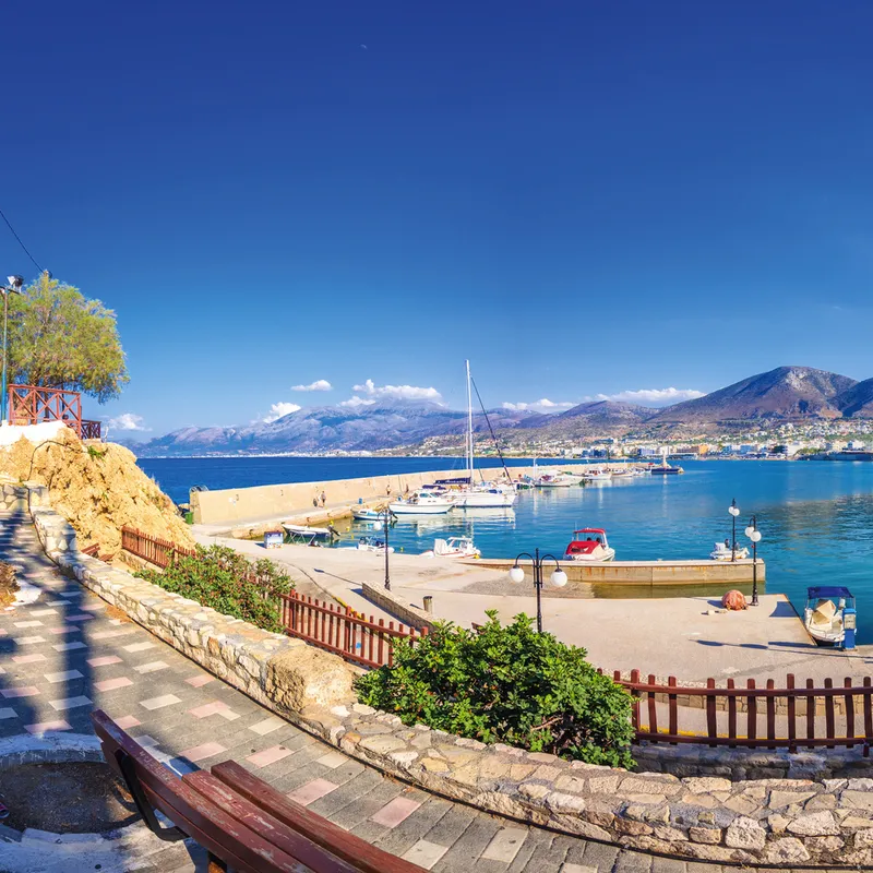 Hafen von Chersonissos auf Kreta mit Booten und hügeliger Landschaft im Hintergrund.