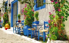 Bunte Tavernen mit blauen Stühlen und Blumen an einer sonnigen Gasse in Kreta, Griechenland.