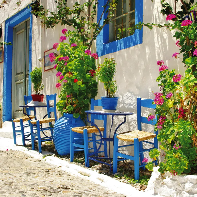 Bunte Tavernen mit blauen Stühlen und Blumen an einer sonnigen Gasse in Kreta, Griechenland.