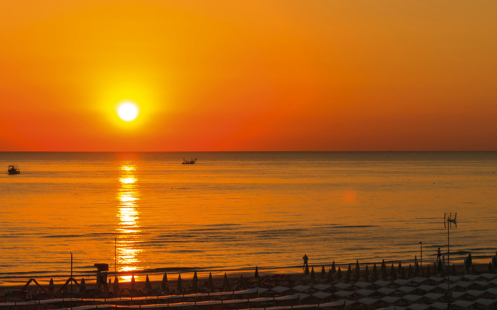 Sonnenuntergang am Strand von Rimini mit Booten am Horizont.