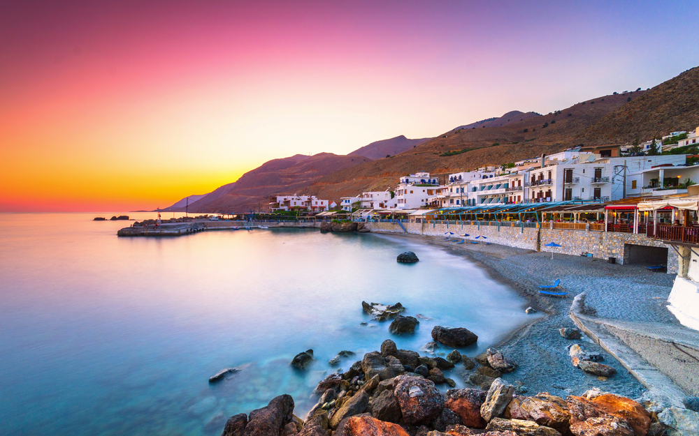 Küstenstadt bei Sonnenuntergang mit Bergen und ruhigem Meer.