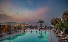 Hotelpool bei Sonnenuntergang mit Liegestühlen und Palmen in Griechenland.