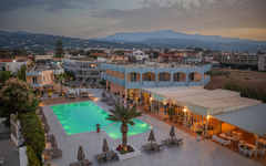 Hotel mit Pool auf Kreta bei Sonnenuntergang, umgeben von Gebäuden und Hügeln.