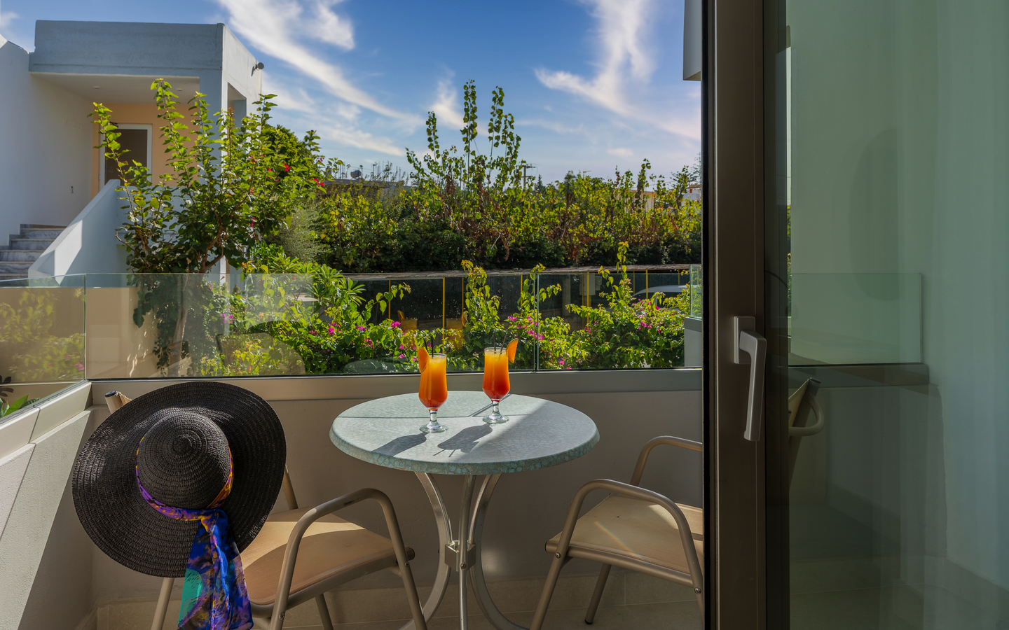 Balkon mit Tisch, zwei Getränken, Sonnenhut, Blick auf Garten und Himmel