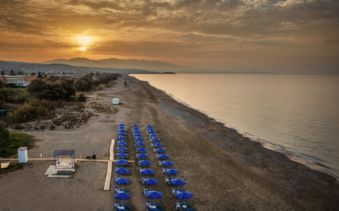 Strand mit blauen Sonnenschirmen und Sonnenuntergang in Kreta, Griechenland.