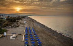 Strand mit blauen Sonnenschirmen und Sonnenuntergang in Kreta, Griechenland.