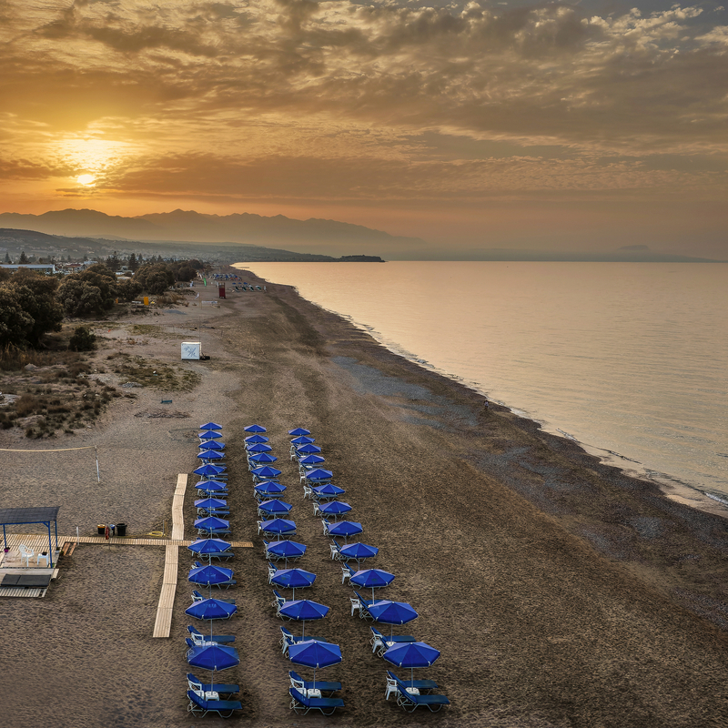 Strand mit blauen Sonnenschirmen und Sonnenuntergang in Kreta, Griechenland.