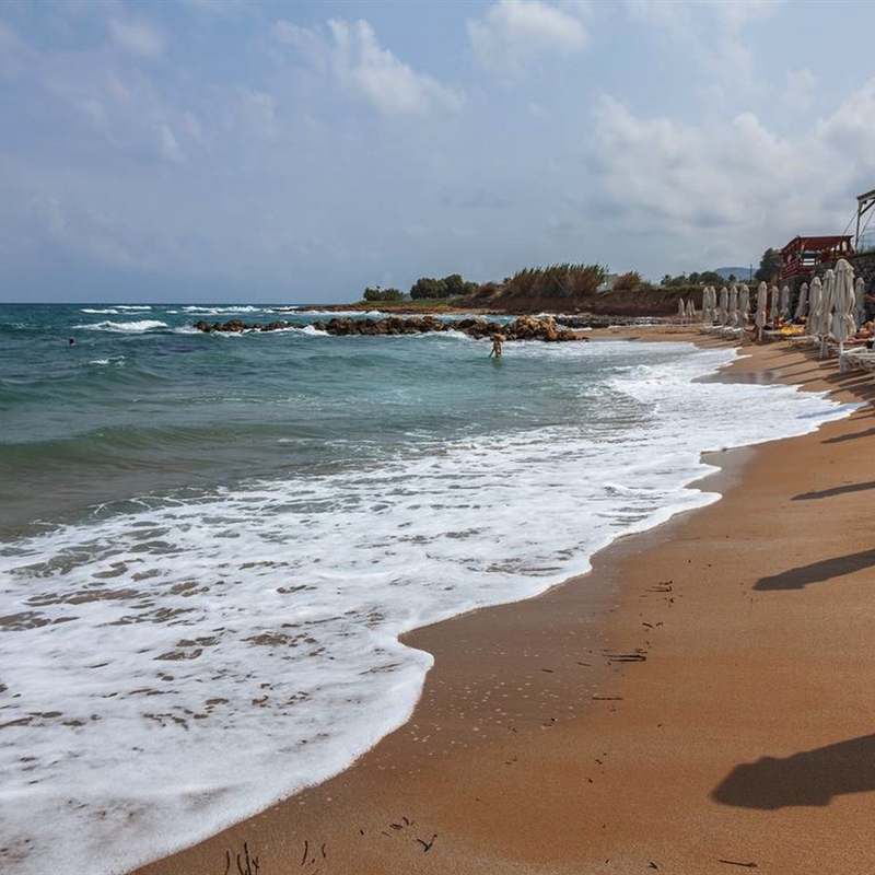 Strand von Rethymno, Kreta, mit Wellen und Liegestühlen im Hintergrund.