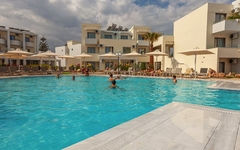 Hotelpool mit Badegästen vor hellen Gebäuden bei bewölktem Himmel.