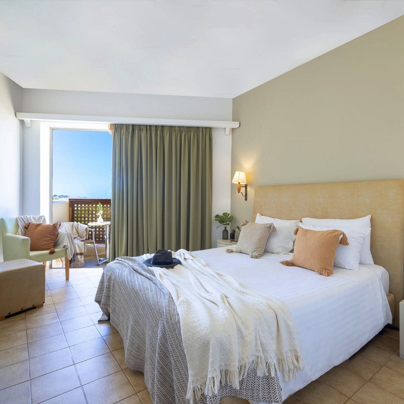 Standardzimmer mit Doppelbett und Blick auf Balkon und Pool.