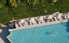 Ein Pool mit Liegestühlen und Sonnenschirmen, umgeben von Grünfläche.