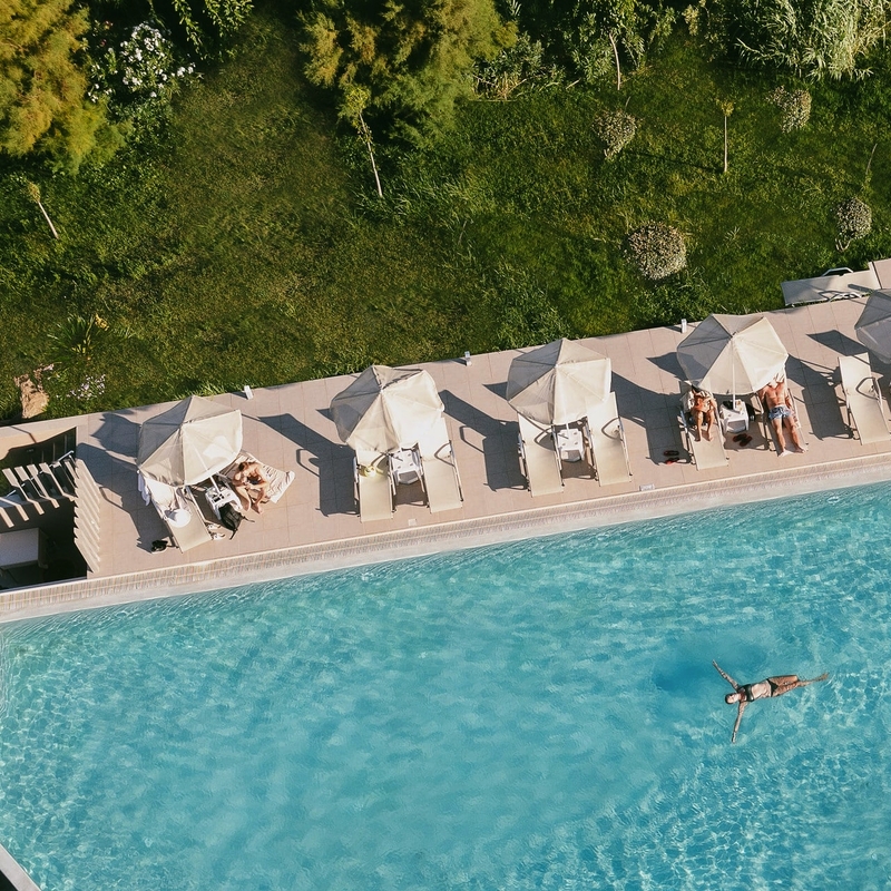 Ein Pool mit Liegestühlen und Sonnenschirmen, umgeben von Grünfläche.