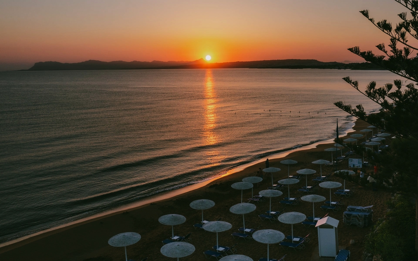 Sonnenuntergang am Strand mit Sonnenschirmen und Meerblick.
