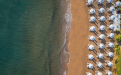 Strand mit Sonnenschirmen und Wellen am Ufer aus der Vogelperspektive.
