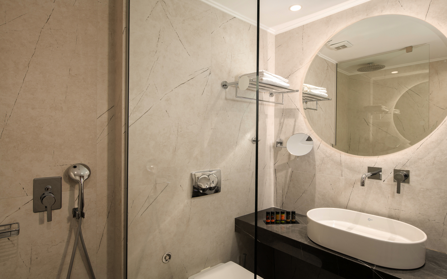 Modernes Hotelbadezimmer mit weißem Waschbecken und runden Spiegel an der Wand.