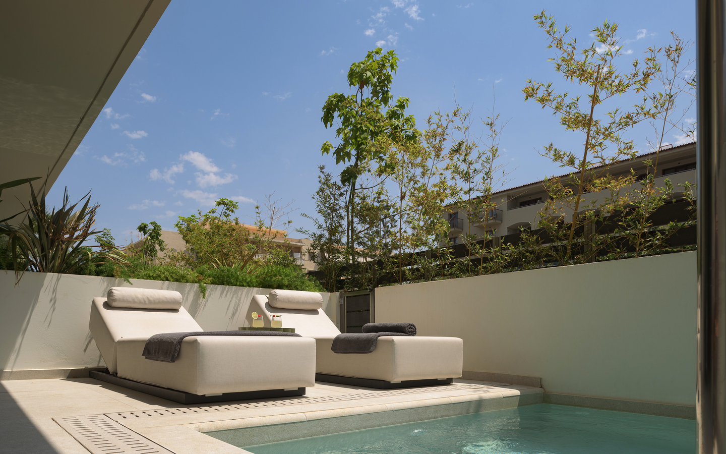 Sonnige Terrasse mit Pool und zwei Liegestühlen im Hotel The Artemis Palace, Kreta.