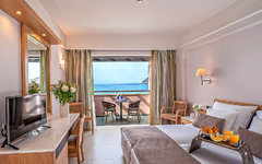 Helles Hotelzimmer mit Doppelbett, TV, Balkon und Meerblick.