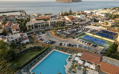 Blick auf ein Hotelresort mit Pool, Tennisplätzen und Meer im Hintergrund.