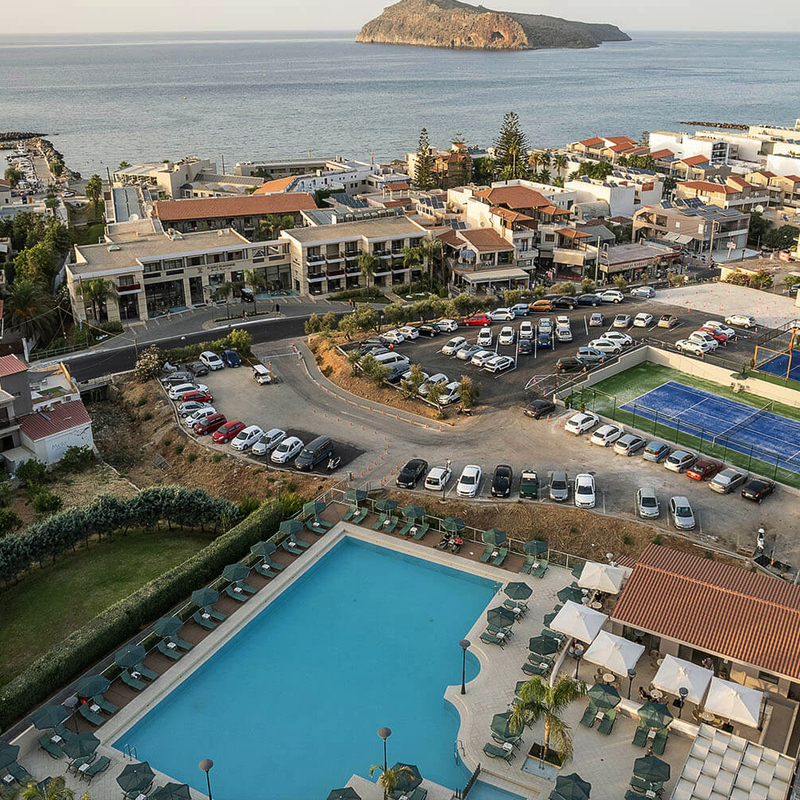 Blick auf ein Hotelresort mit Pool, Tennisplätzen und Meer im Hintergrund.