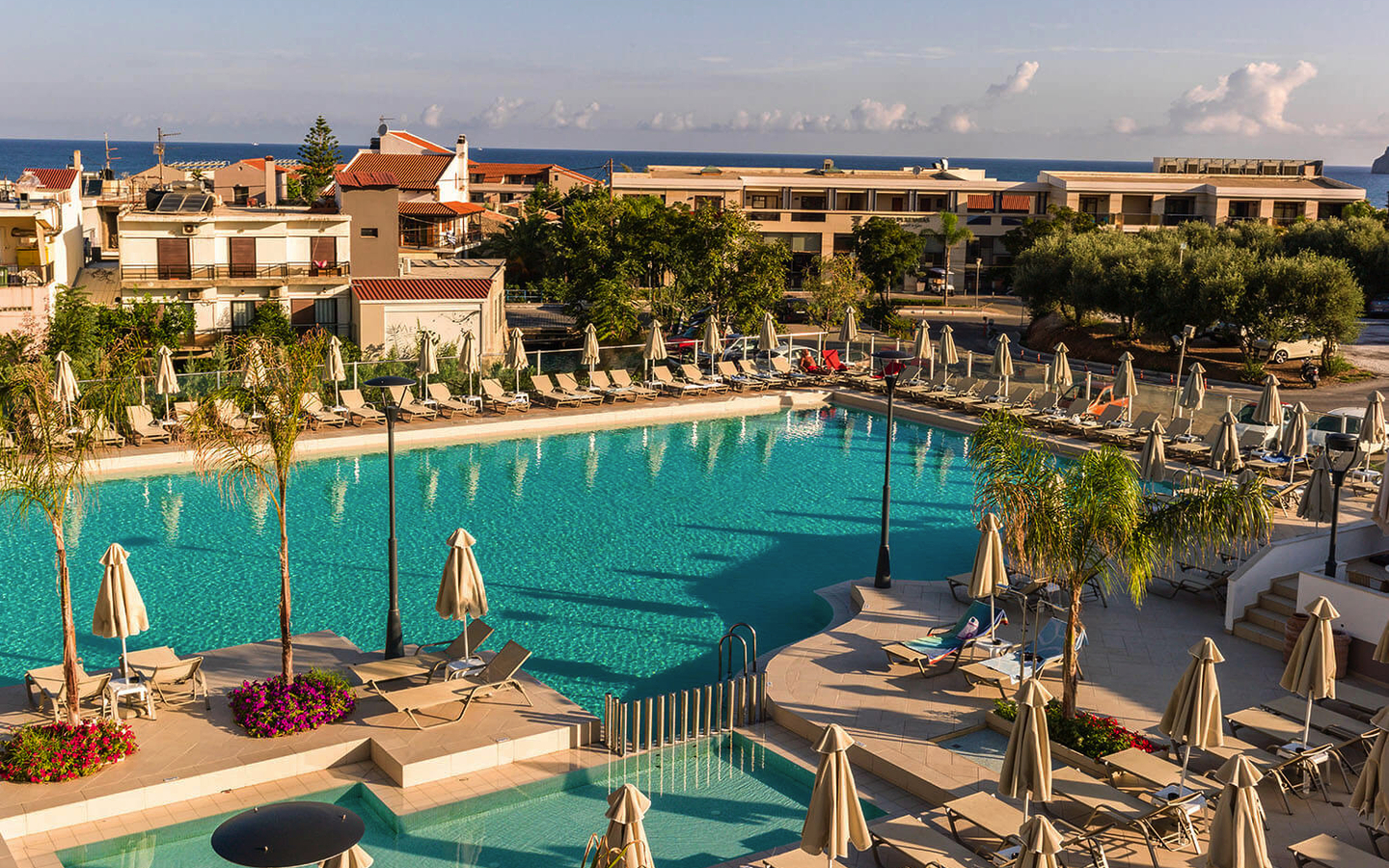 Poollandschaft im Hotel Porto Platanias Village Resort auf Kreta, umgeben von Liegestühlen.