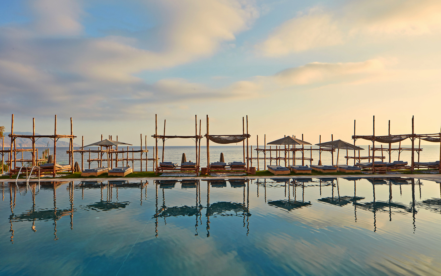 Pool mit Liegestühlen und Sonnenschirmen am Hotel La Mer in Kreta bei Sonnenuntergang.
