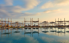 Pool mit Liegestühlen und Sonnenschirmen am Hotel La Mer in Kreta bei Sonnenuntergang.