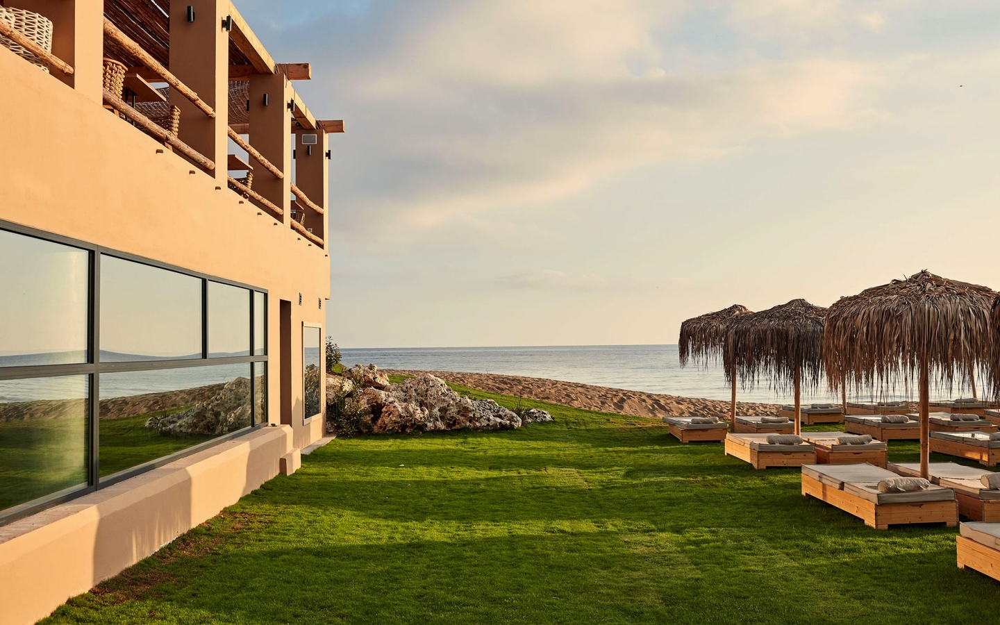 Hotel mit Rasenfläche, Liegen und Meerblick bei Sonnenuntergang auf Kreta.