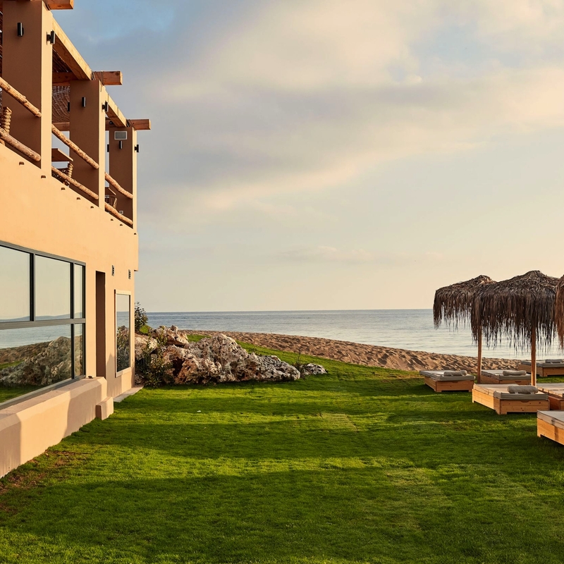 Hotel mit Rasenfläche, Liegen und Meerblick bei Sonnenuntergang auf Kreta.