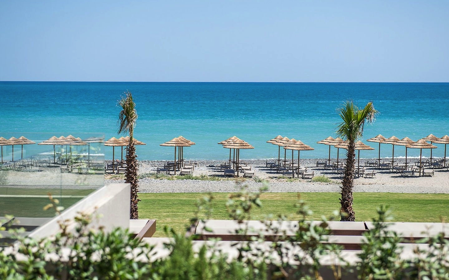Strand mit Sonnenschirmen und klarem blauen Meer im Hintergrund.