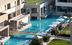 Poolbereich eines modernen Resorts mit Liegen und Sonnenschirmen, umgeben von Grünflächen.