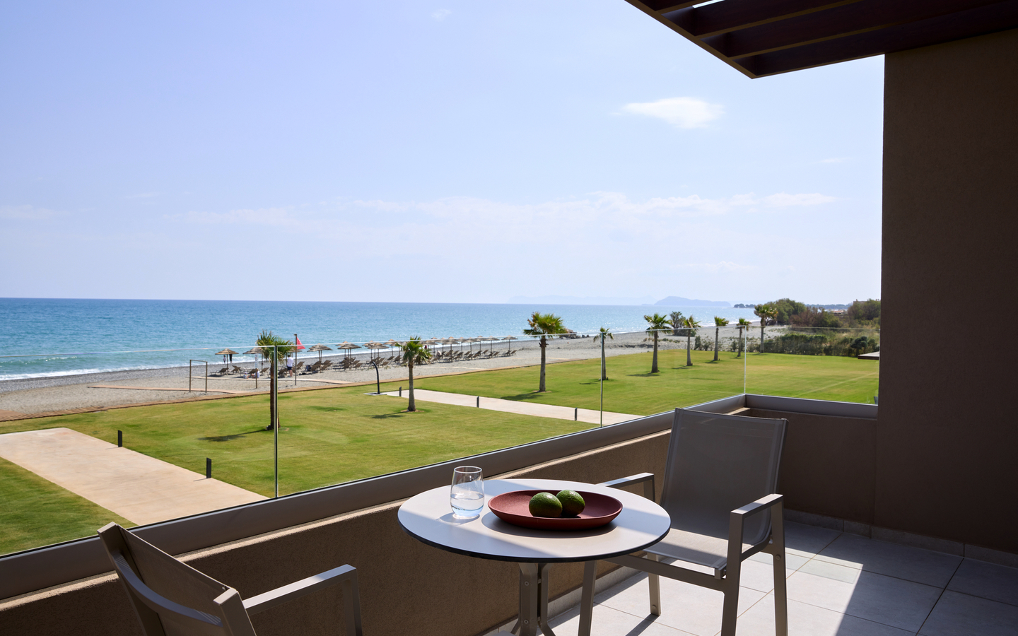 Balkon mit Meerblick und Strand, zwei Stühle, Tisch mit Obst und Glas