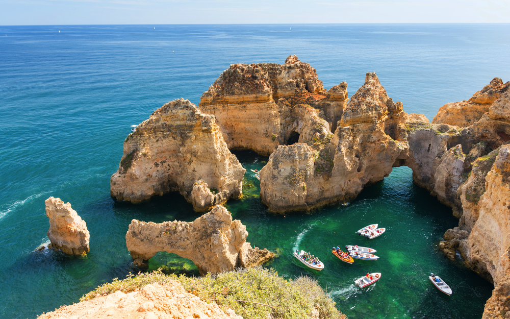 Boote im türkisfarbenen Meer vor der felsigen Küste von Lagos, Algarve.