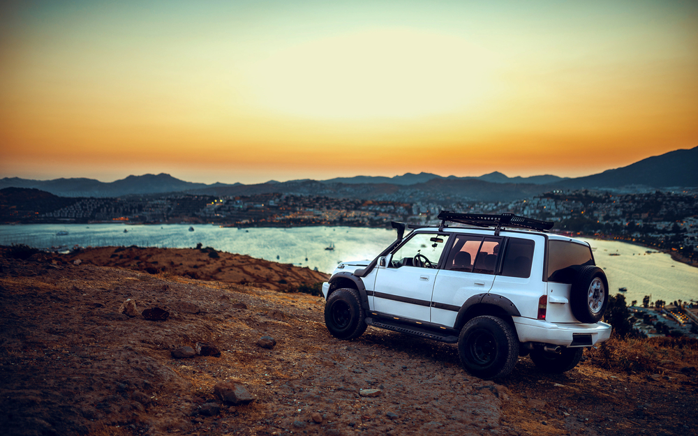 Geländewagen auf Hügel bei Sonnenuntergang mit Blick auf Küste und Stadt in Bodrum
